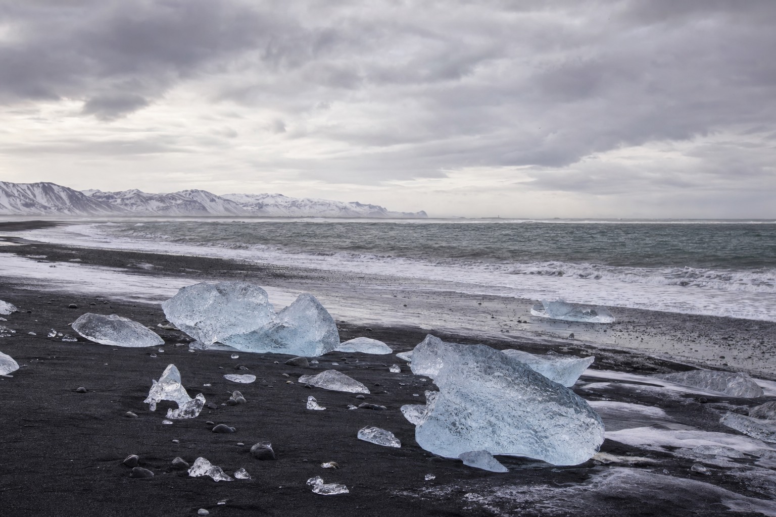 Windswept black sand and stranded ice at the edge of south-east Iceland under a fast-moving grey sky