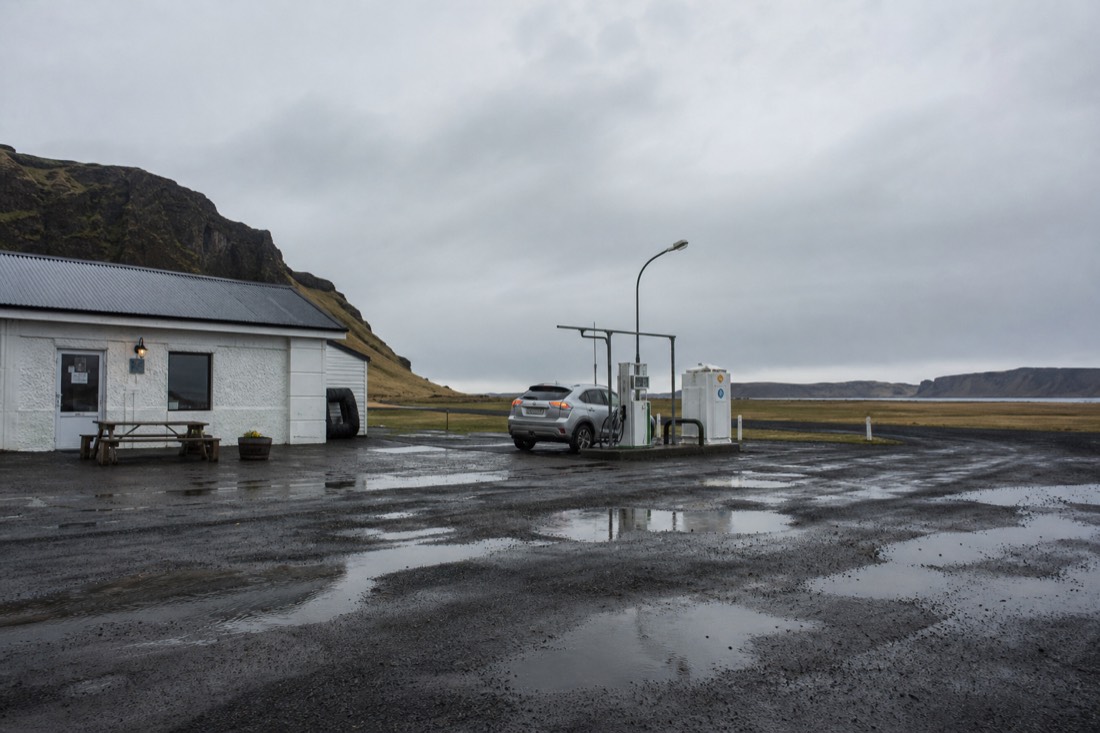 A rural fuel station and small cafe on Iceland's south coast Route 1 under a grey sky, with a car refuelling