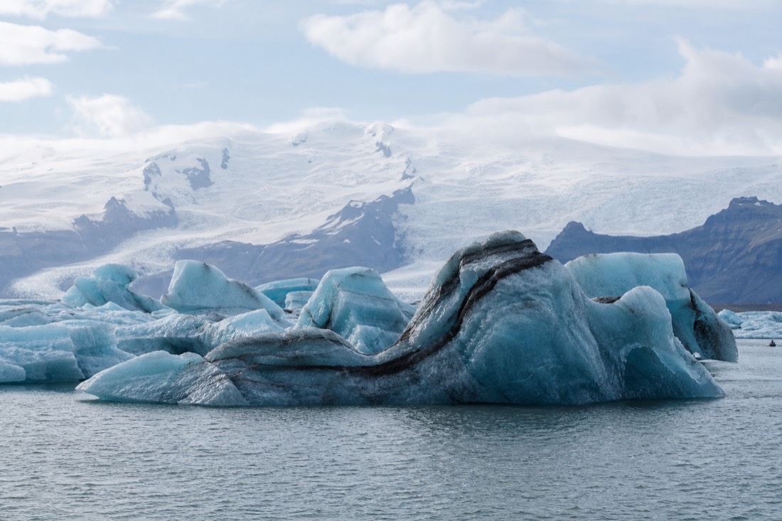 Deep blue icebergs with dark ash stripes floating on Jökulsárlón under a bright sky