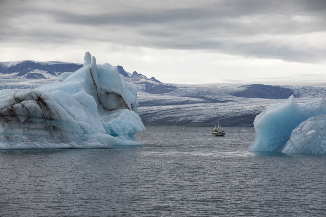 A small boat moving between large icebergs on Jökulsárlón with the glacier visible behind