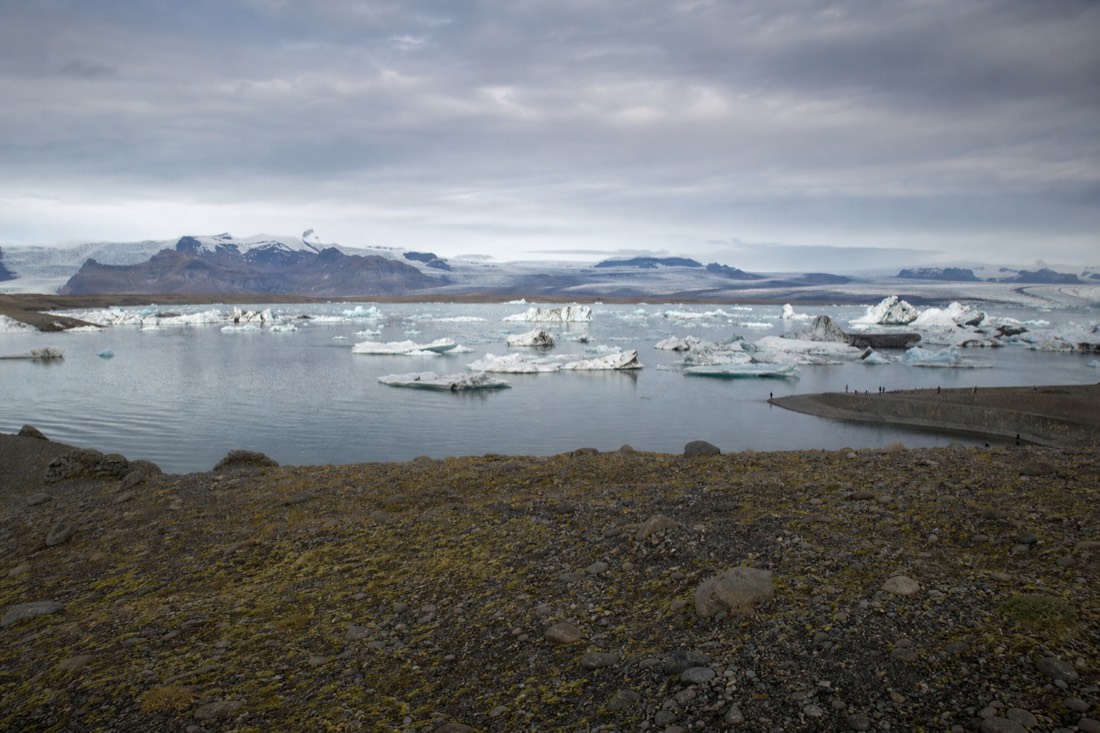 Visitors standing well back from the shoreline at a Jökulsárlón viewpoint in soft low-angle light