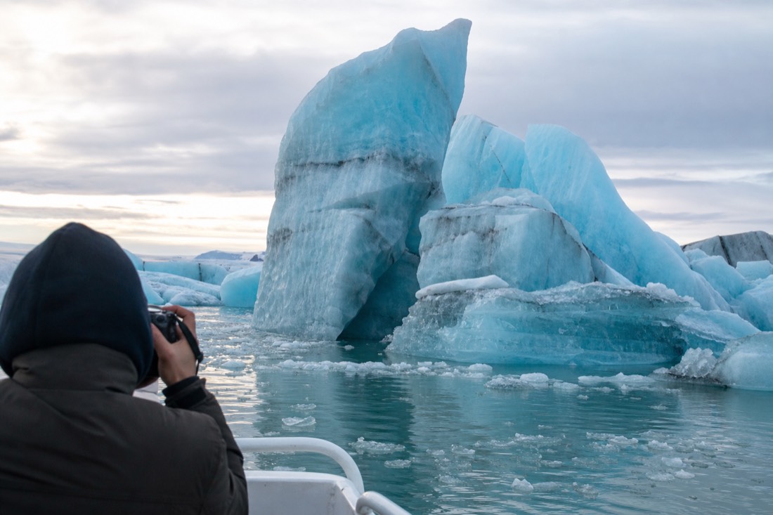 Visitor photographing towering blue icebergs from a boat on Jökulsárlón Glacier Lagoon in soft Icelandic light