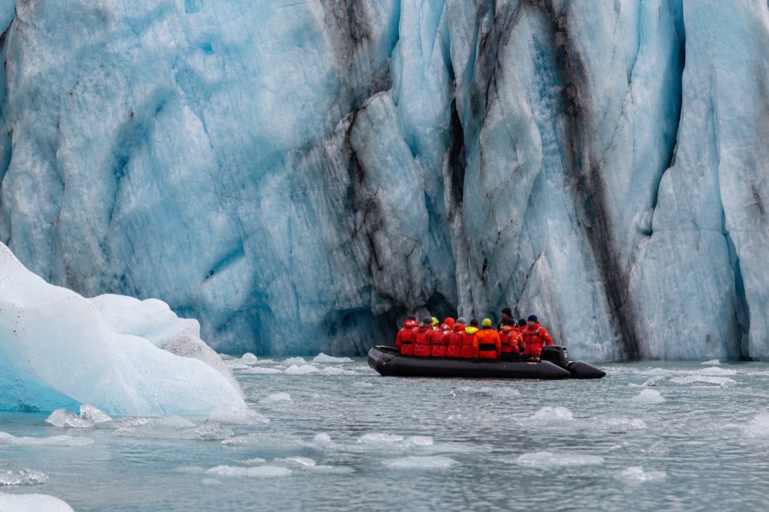 Black Zodiac inflatable boat with passengers in flotation suits close to the blue glacier face on Jökulsárlón Glacier Lagoon