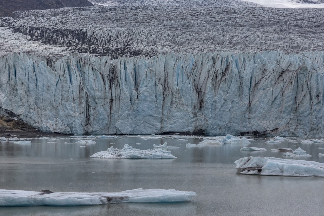The glacier wall of Fjallsjökull rising close behind the small, quiet Fjallsárlón lagoon with a scatter of icebergs