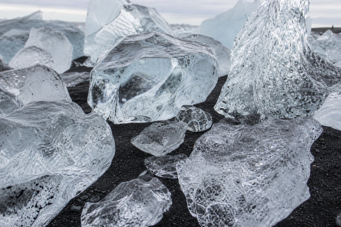 Close view of clear glacier ice chunks on black sand at Fellsfjara, the stretch known as Diamond Beach in South-East Iceland