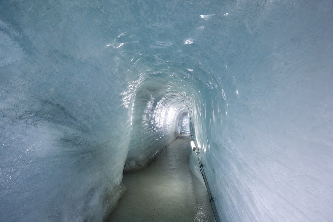 Interior of the man-made Langjökull ice tunnel in Iceland with smooth lit walls of pale blue ice